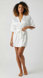 Robe curto de cetim branco feminino, com faixa na cintura e mangas amplas, brilho acetinado em luz suave.