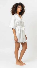 Robe curto de cetim branco feminino, com faixa na cintura e mangas amplas, brilho acetinado em luz suave.