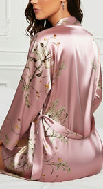 sentada na cama conjunto rosa em cetim floral look confortável para noite e rotina de beleza