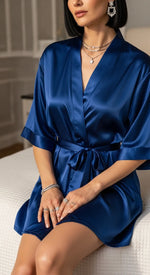 robe curto azul feminino - sentada na cama em outra pose, foco na amarração e gola em V